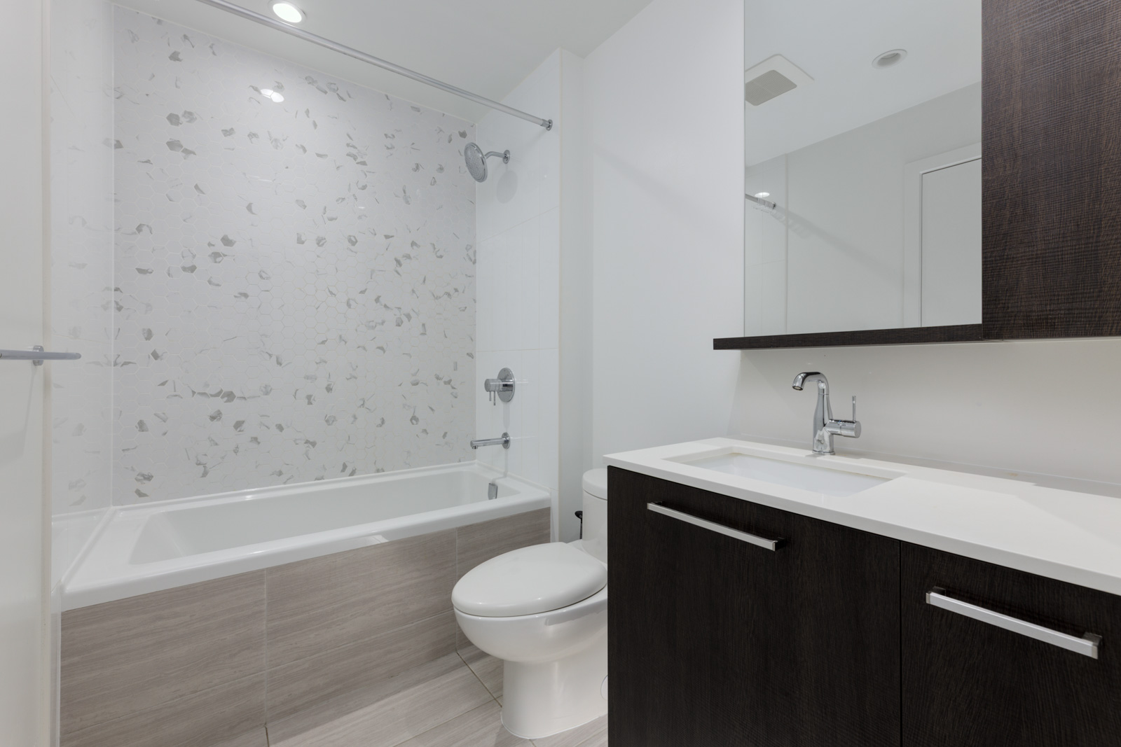 Modern Coquitlam bathroom with bathtub, shower, white sink countertop, dark wood vanity, toilet, and tiled floor and walls.