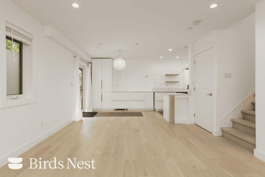 Bright, modern open-plan kitchen and living area with wood floors, white walls, large windows, and stairs, in Vancouver near E 8th Ave and St Catherines St.