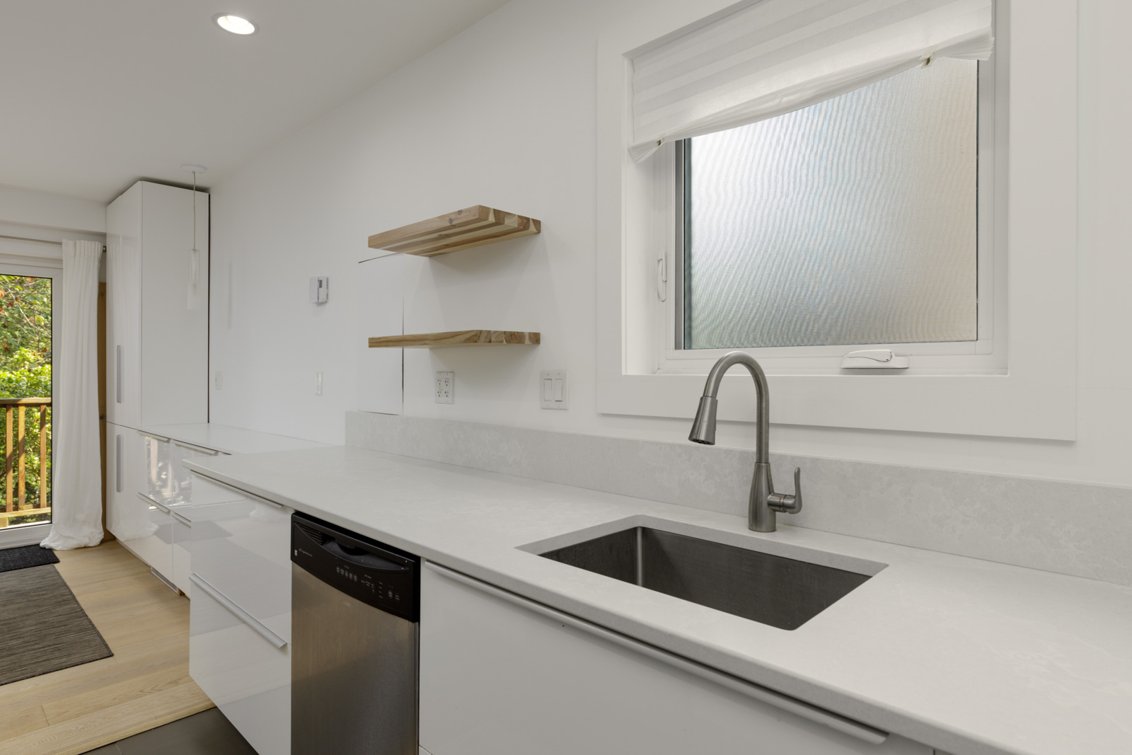 Bright white Vancouver kitchen with stainless sink, faucet, dishwasher, open shelves, and window above the counter.