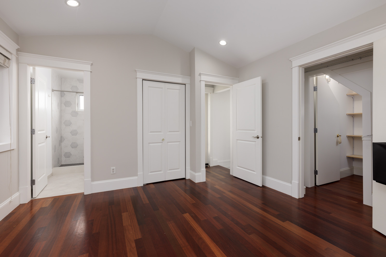 Empty room with dark hardwood floors, white walls, two open doors, closet with double doors, and adjacent bathroom; Vancouver.