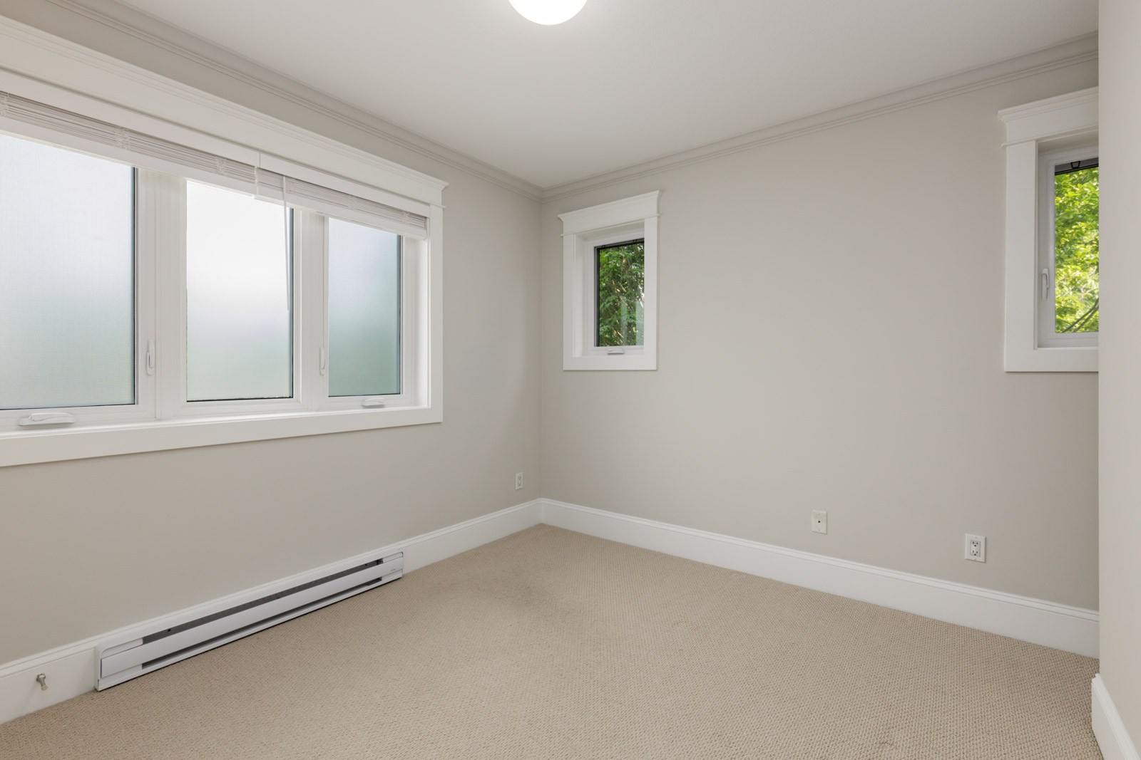 Empty room in Vancouver with beige carpet, off-white walls, three windows with white trim, and a baseboard heater.