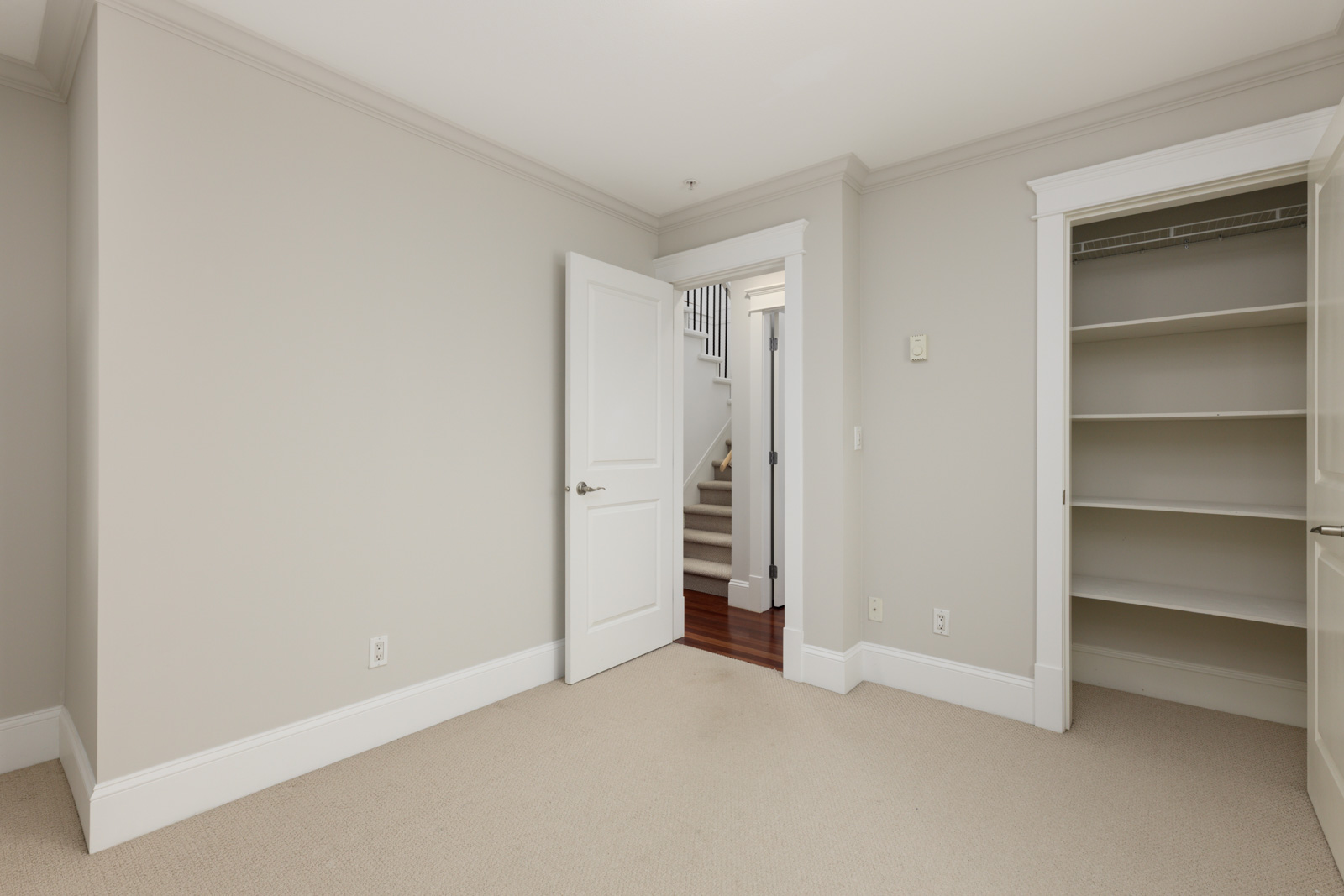 Beige room with open closet, white trim, and open door to hall with stairs; near E 8th Ave and St Catherines St, Vancouver.