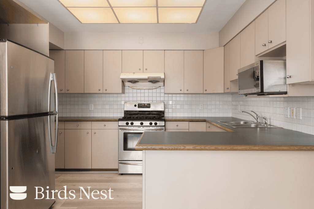 Modern kitchen on W 50th Ave with beige cabinets, stainless appliances, tiled backsplash, wood-trimmed counters, and Birds Nest logo.