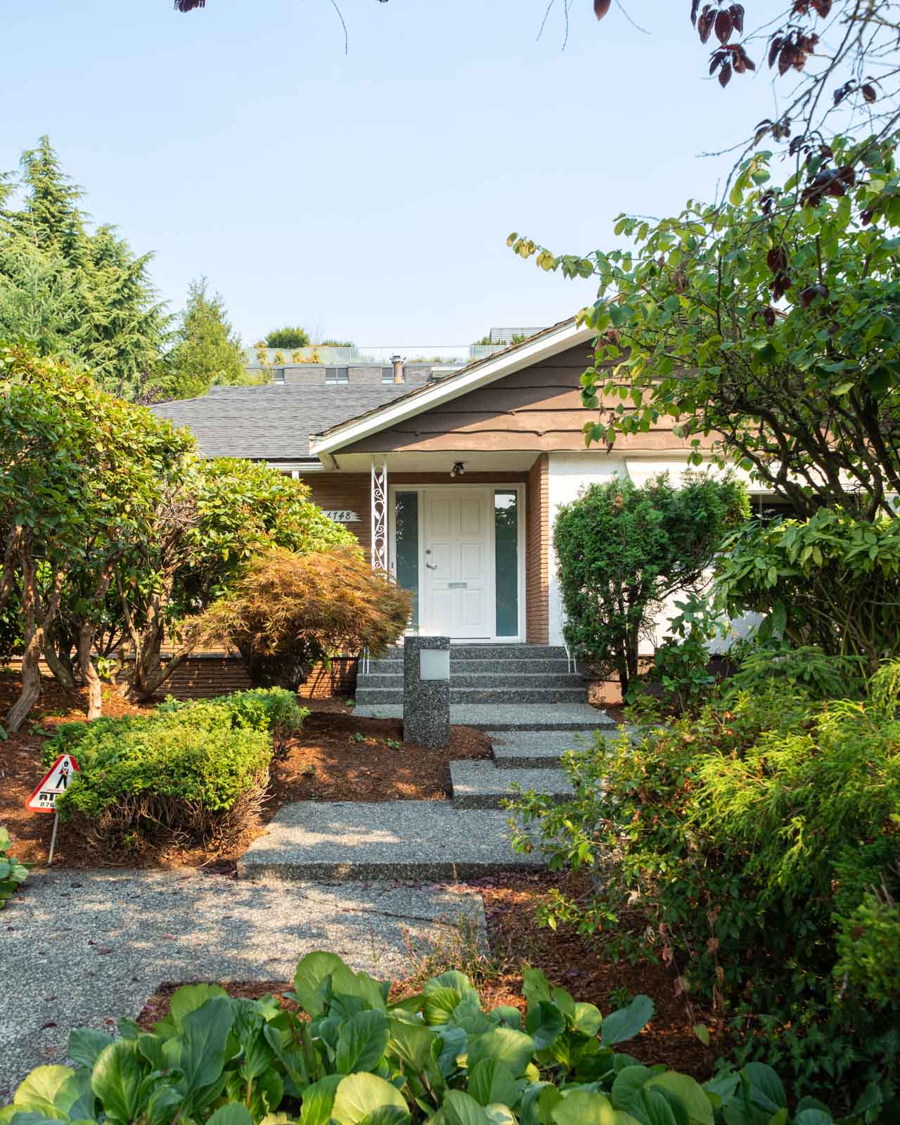 A small house with a white front door on W 50th Ave and Ash St, Vancouver, with steps through a garden and gravel path.