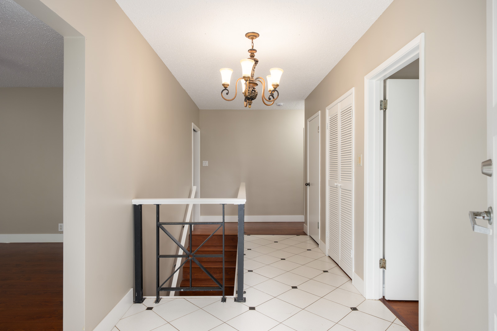 Hallway with beige walls, white doors, black and white tile floor, chandelier, and metal-railed stairs in an Ash Street multi-family home.