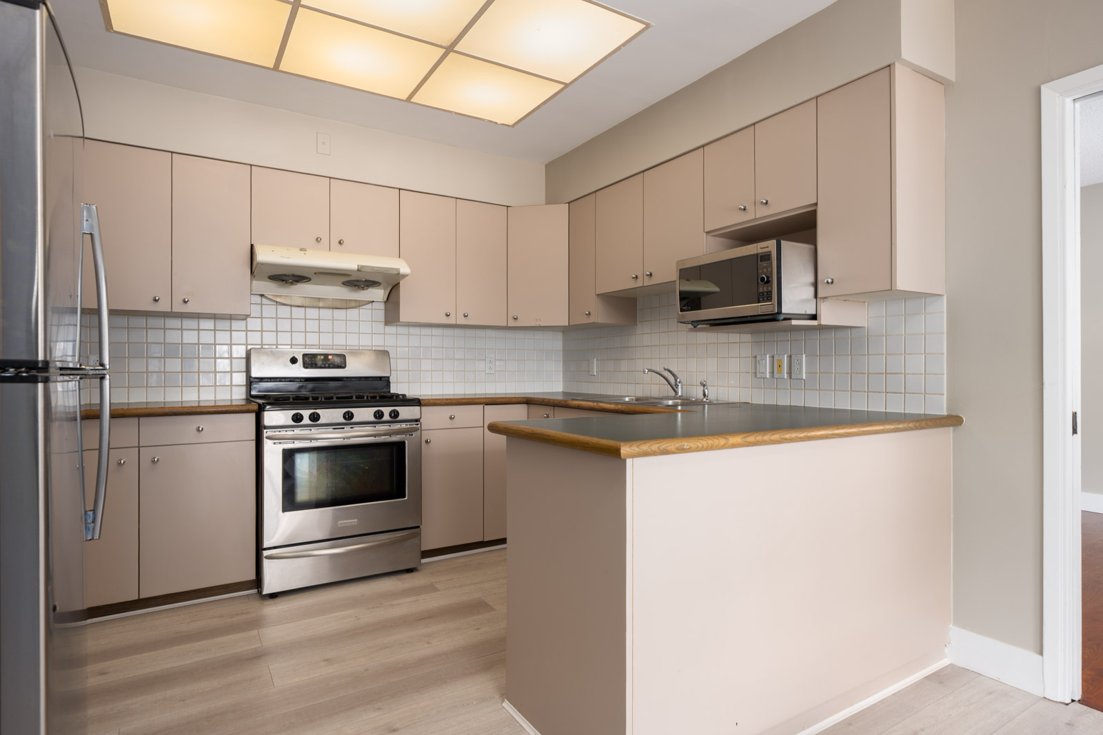 Modern kitchen in Vancouver near W 50th Ave and Ash St with beige cabinets, wood counters, stainless stove, microwave, and tile backsplash.