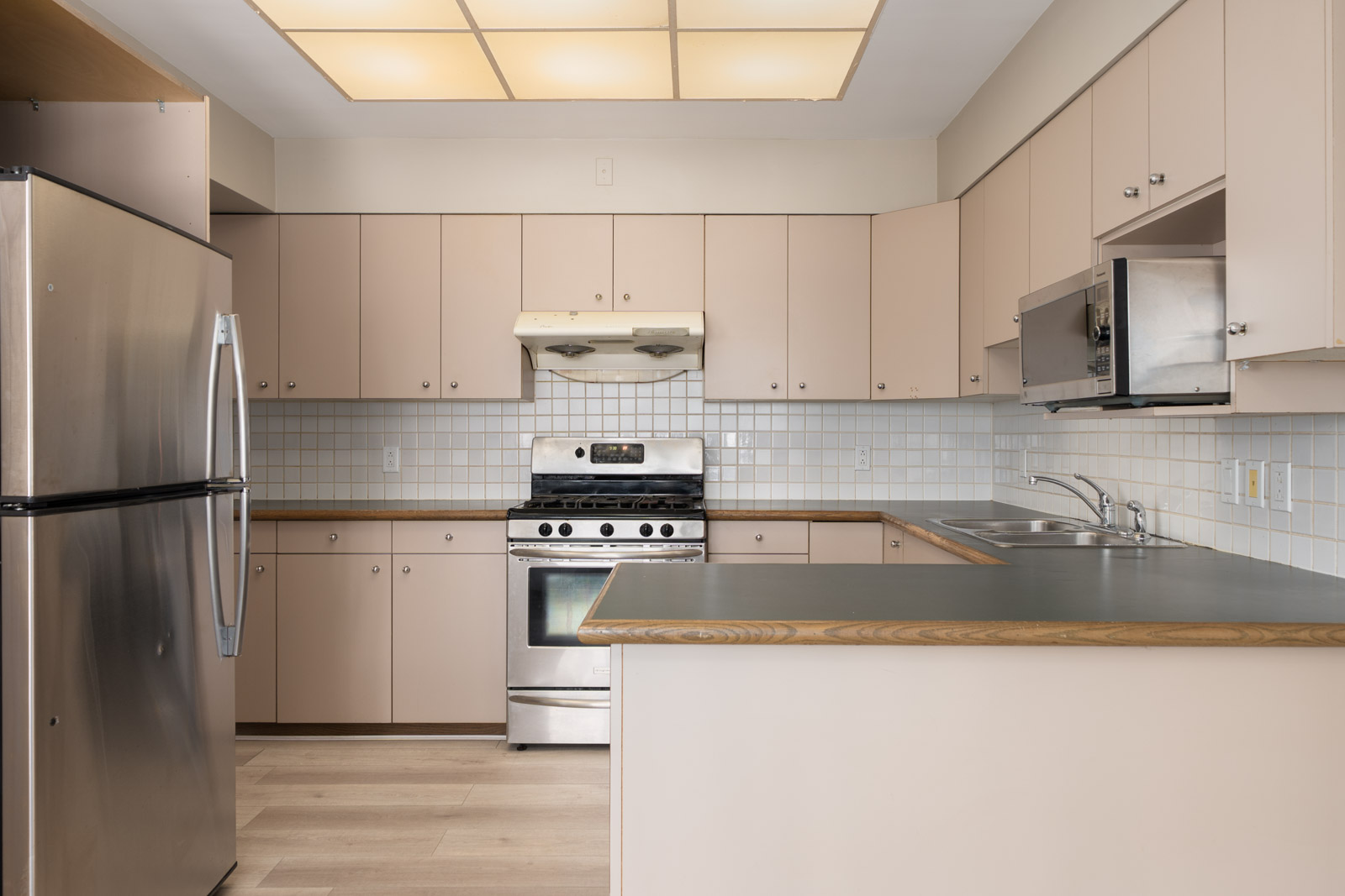 Kitchen with beige cabinets, stainless steel appliances, tiled backsplash, double sink, and large light fixture near Vancouver’s W 50th Ave and Ash St.