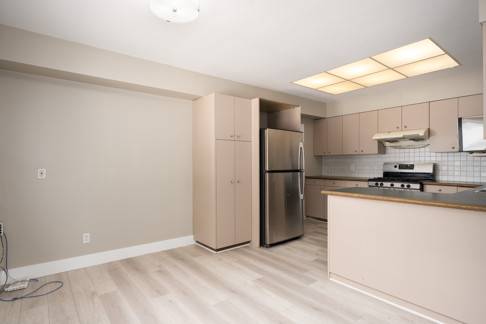 Modern kitchen with light beige cabinets, stainless appliances, tile backsplash, and wood floors in Vancouver near Ash Street.
