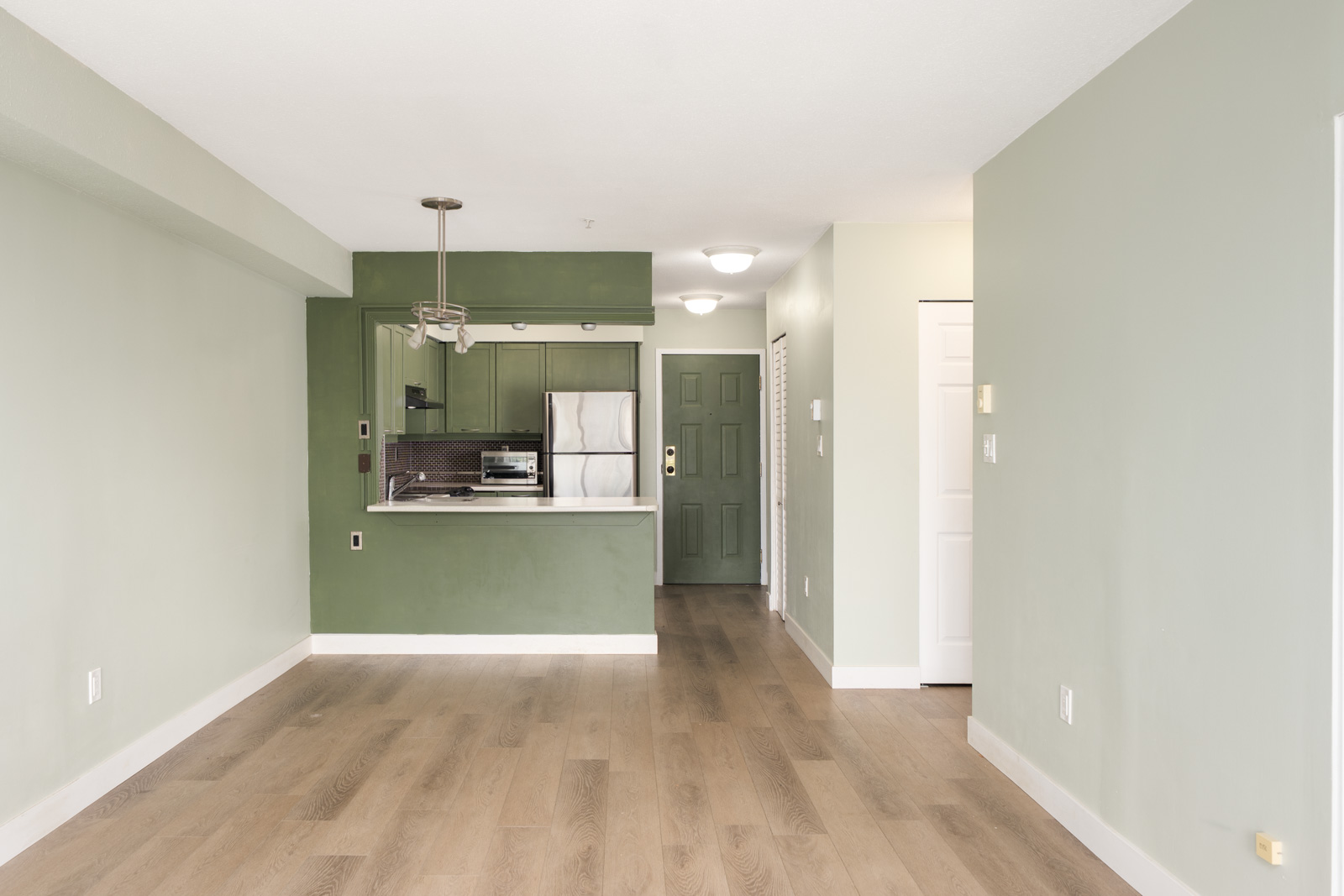 Unfurnished apartment at 1099 E Broadway, Vancouver, with light green walls, wood floors, and a small kitchen in back.