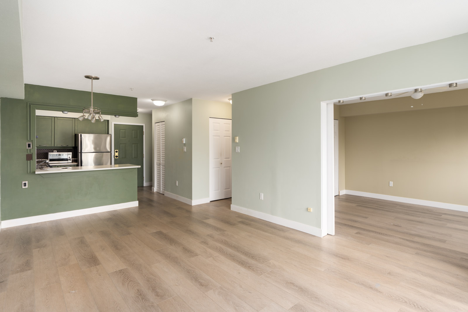 Empty apartment at 1099 E Broadway, Vancouver with light wood floors, green and beige walls, and stainless steel appliances.