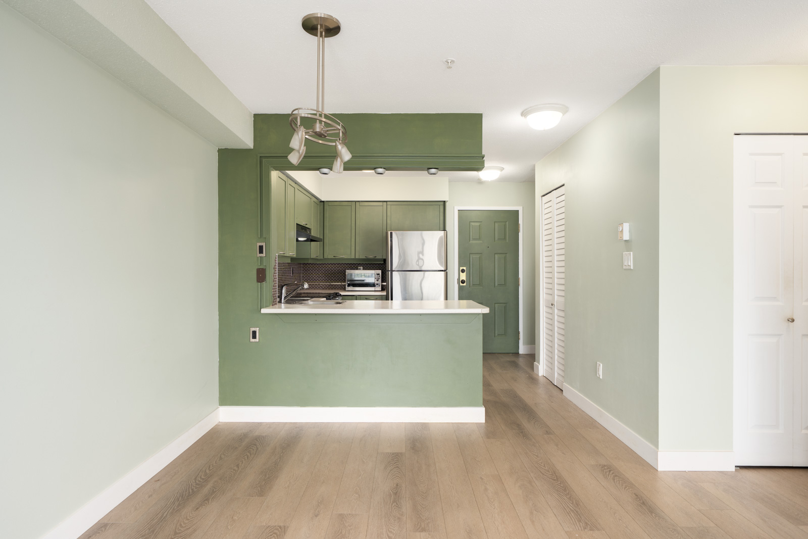 Modern kitchen with green cabinets, stainless appliances, white countertop, light wood floors, and green accent wall in Vancouver.