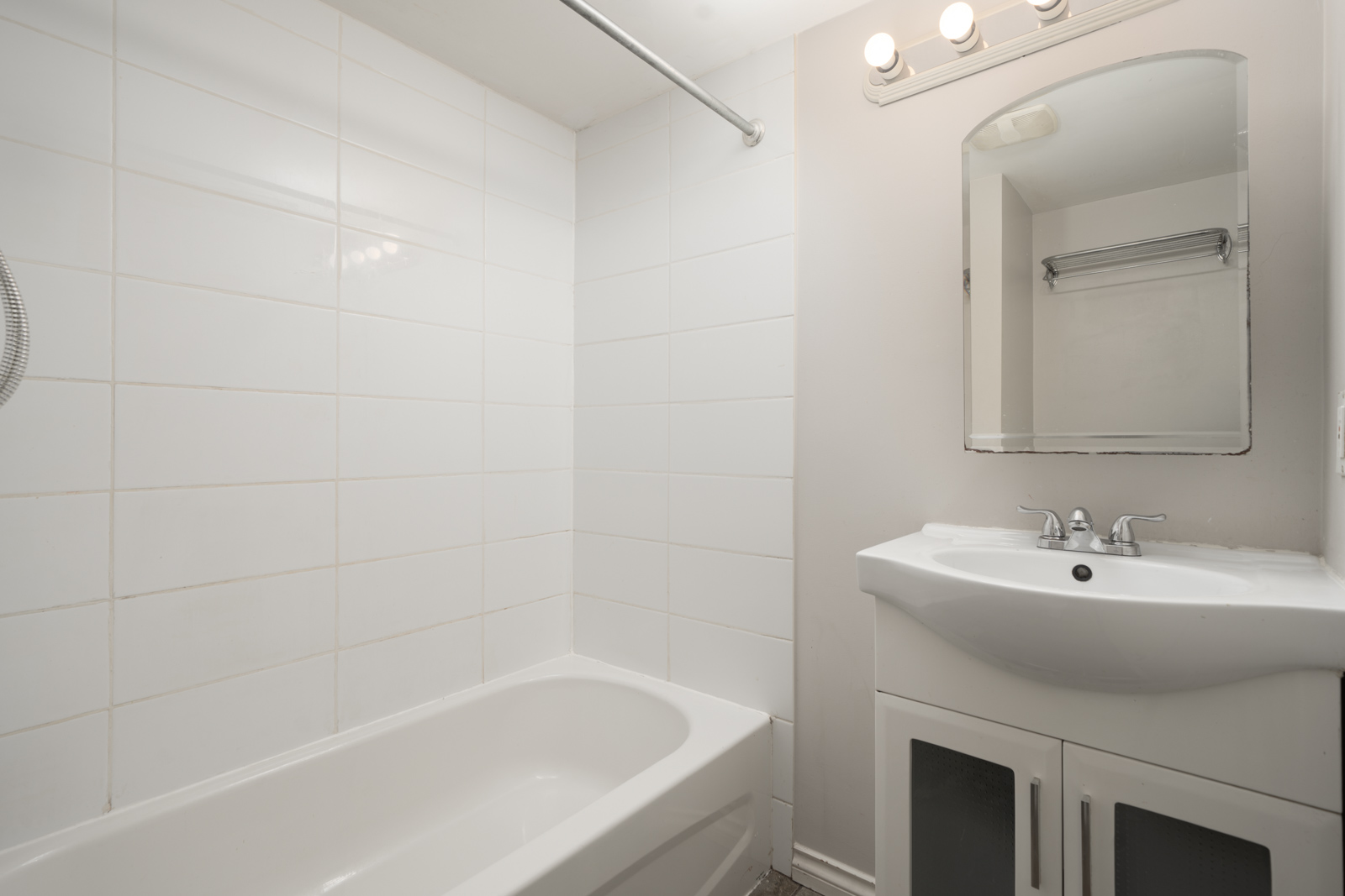 White bathroom with bathtub, tiled shower wall, sink cabinet, mirror, and three-bulb light on 2nd floor in Vancouver residence.