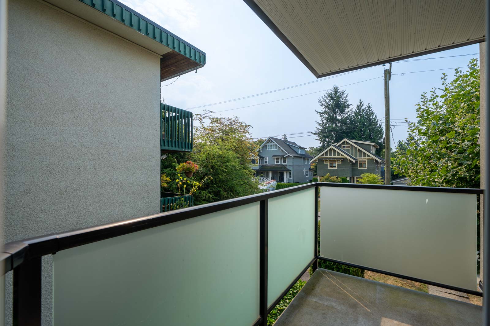 Second-floor balcony with frosted glass railing overlooks trees and houses on a residential street in Vancouver.