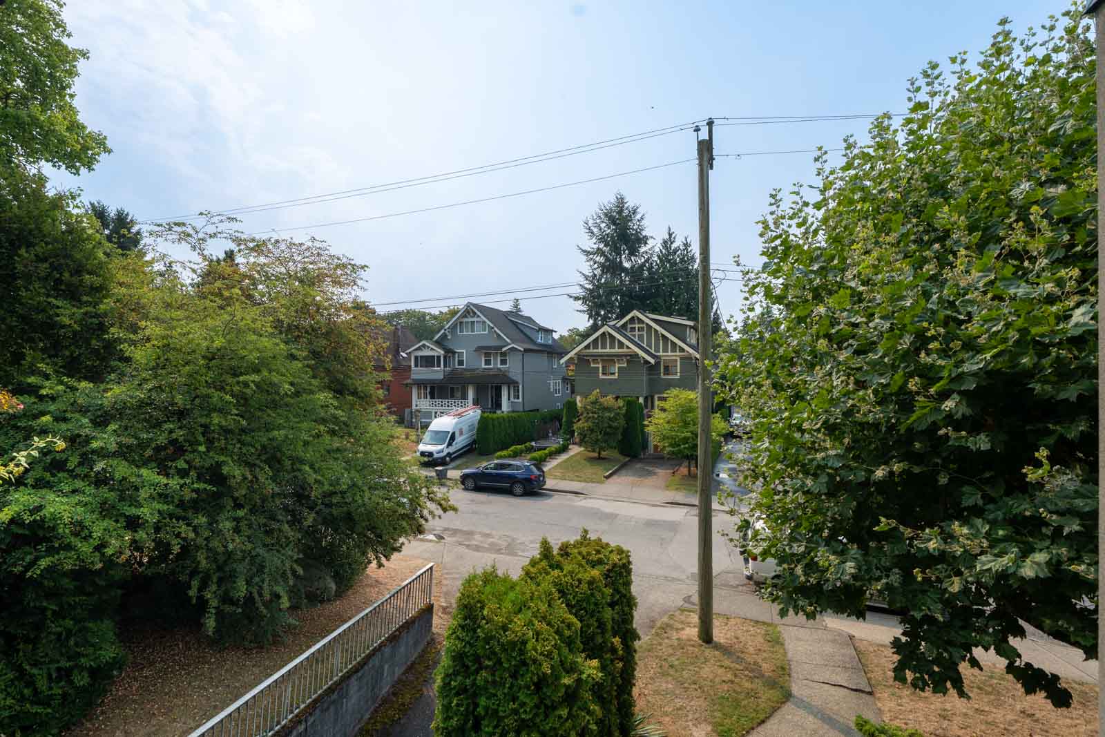 West 5th Avenue in Vancouver with parked cars, green trees, two gray houses (one two-story), utility pole, and wires under clouds.