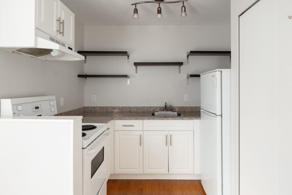 Compact kitchen with white cabinets, electric stove, fridge, single sink, open shelves, hardwood floor; 2nd floor West 5th Ave, Vancouver.