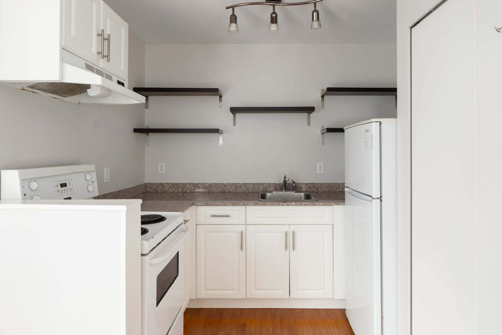 Compact kitchen with white cabinets, electric stove, fridge, single sink, open shelves, hardwood floor; 2nd floor West 5th Ave, Vancouver.