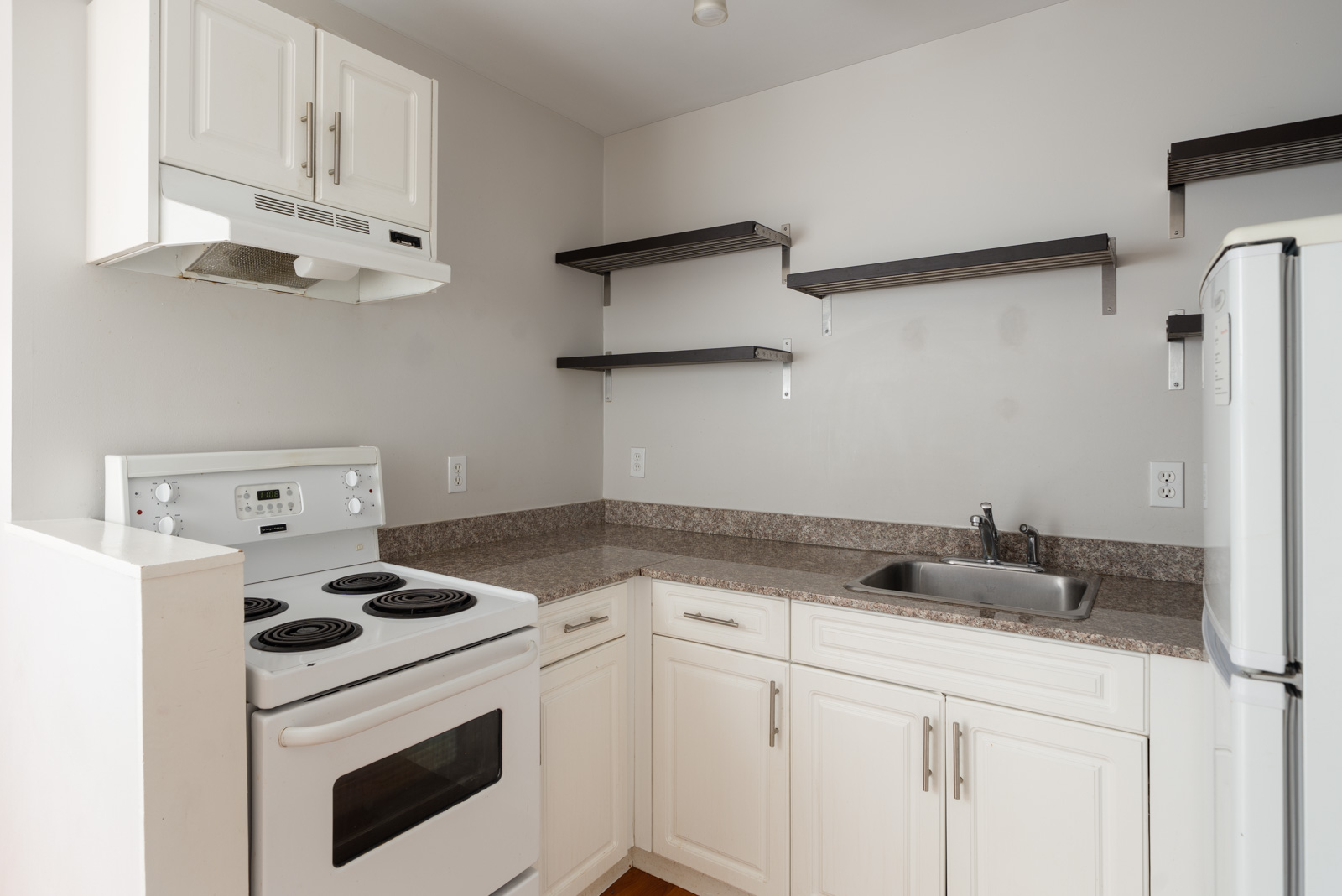 Small kitchen on 2nd floor in Vancouver with white cabinets, electric stove, fridge, sink, brown counters, and two dark shelves.