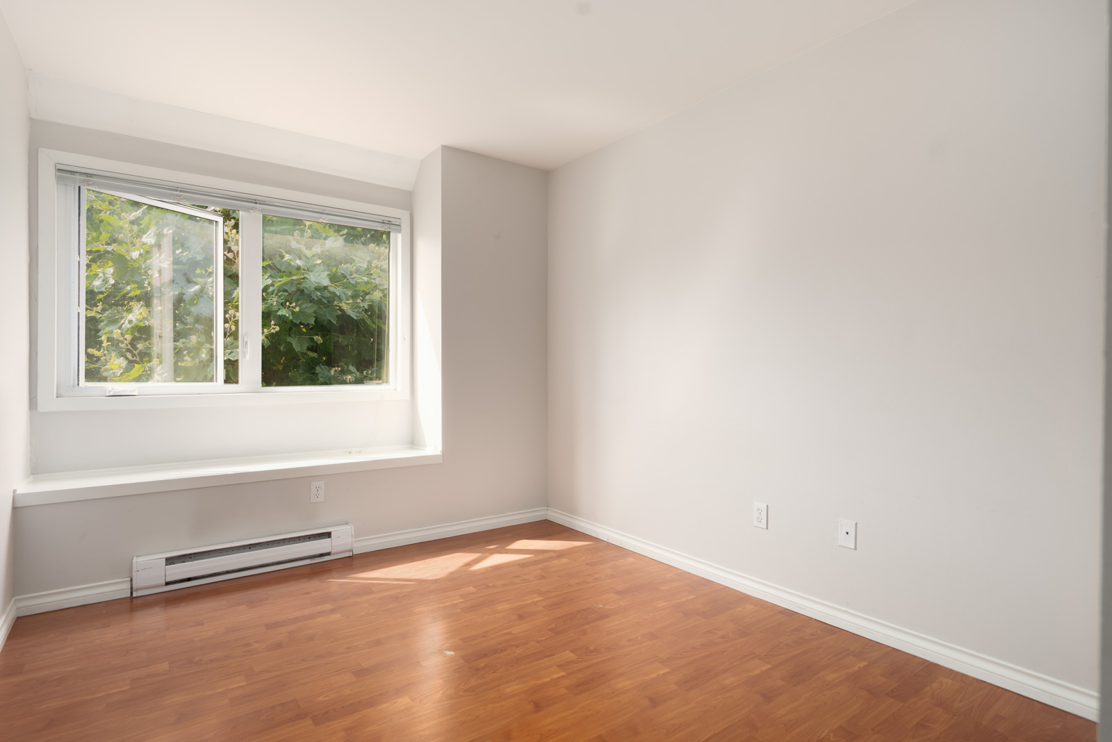 Sunlit empty room with light walls, wood floor, open window, and white heater on 2nd floor at 2365 West 5th Ave, Vancouver.