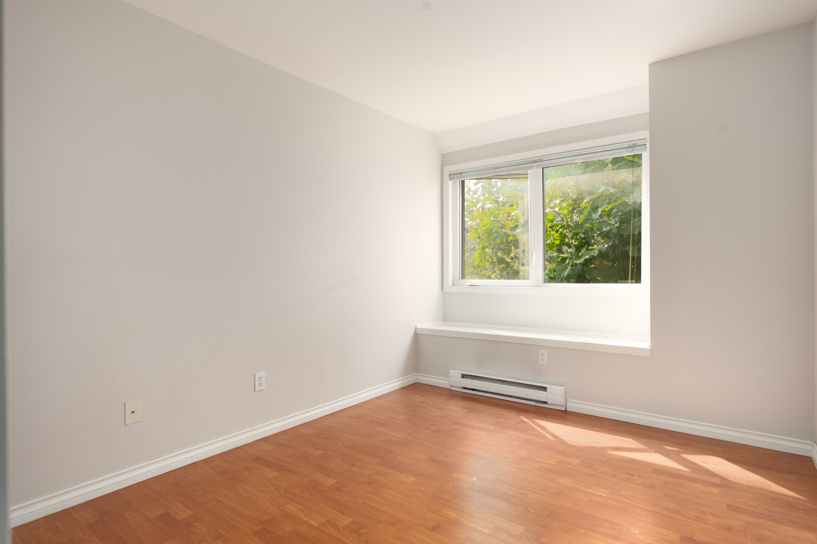 Empty room on 2nd floor at 2365 West 5th Ave, Vancouver; light gray walls, wood floor, large window with greenery, window bench.