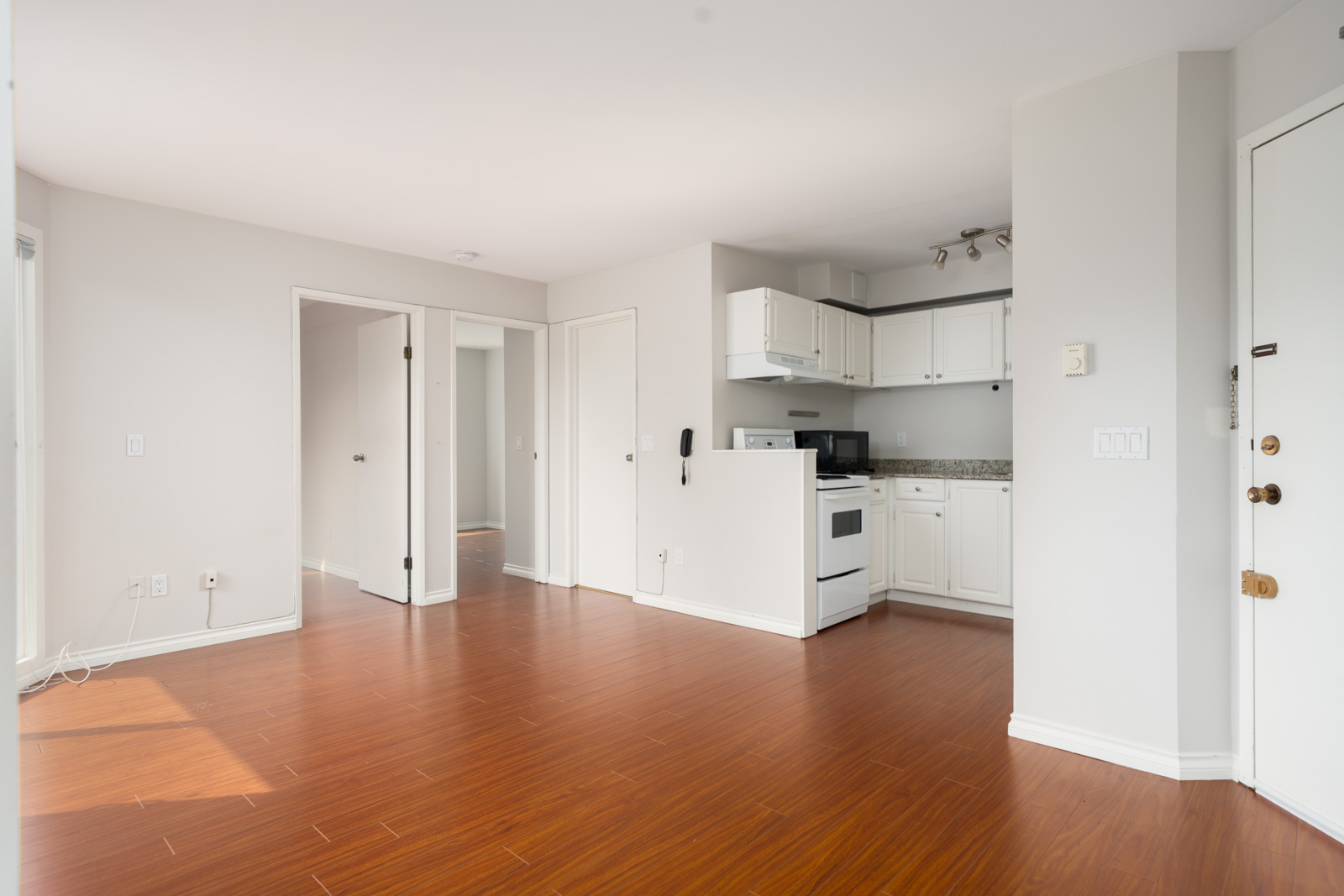 Unfurnished apartment with wood floors, white walls, small kitchen, open living area; 3rd floor, Vancouver. Two doorways, white front door.