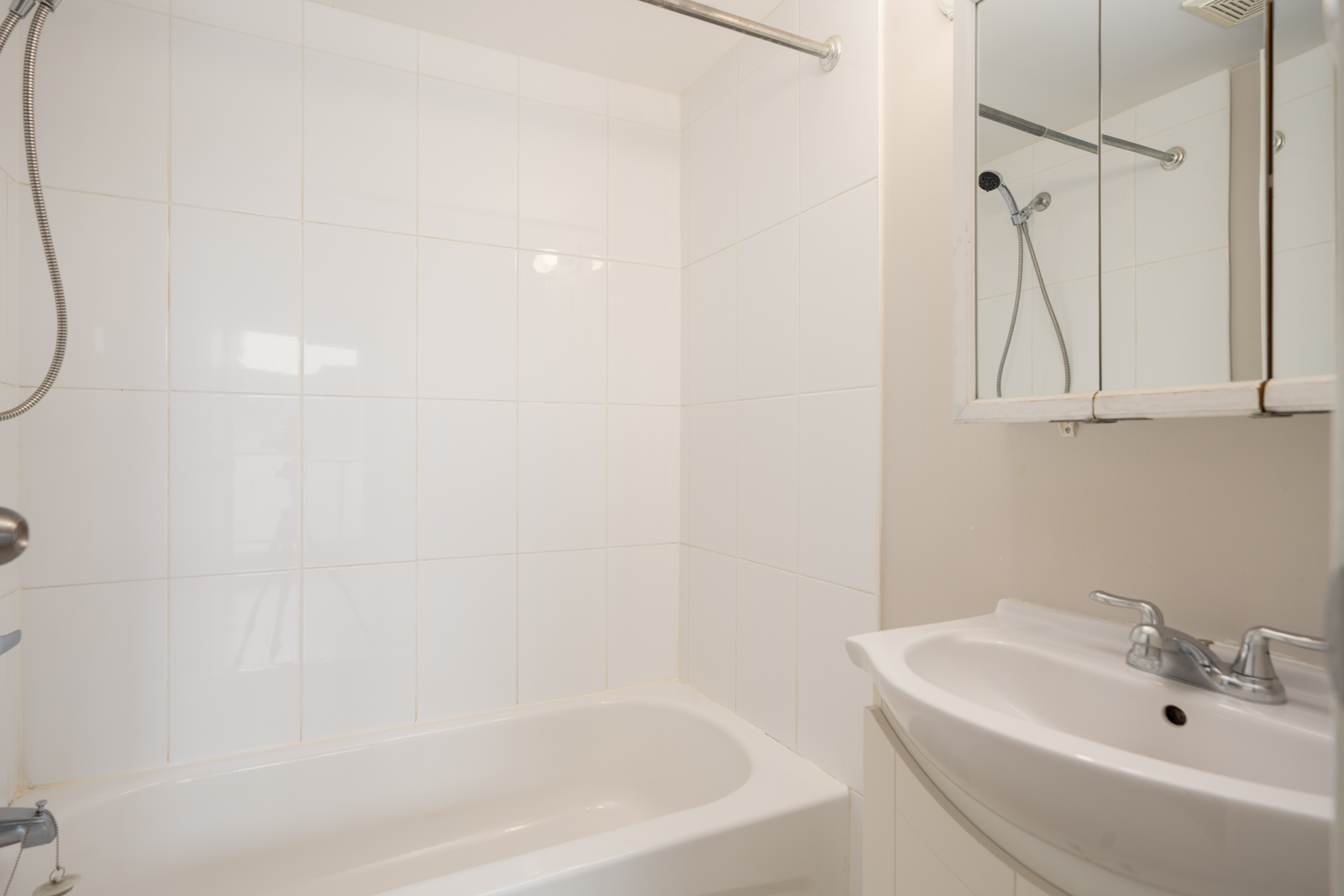 White bathroom on 3rd floor, 2365 West 5th Ave, Vancouver, with tiled tub-shower combo, showerhead, mirror, and chrome sink.