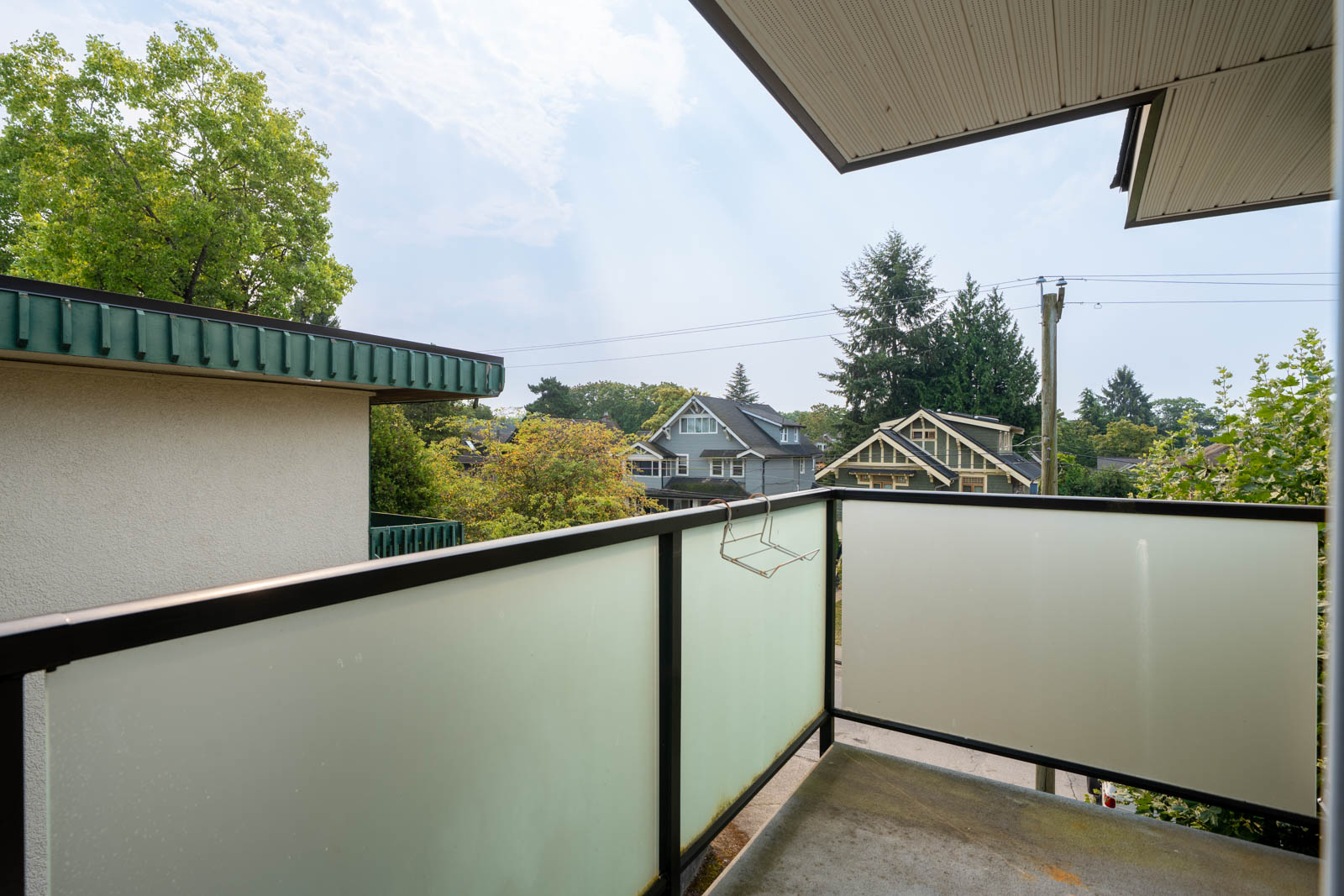 Small 3rd floor balcony with frosted glass railing, overlooking houses, trees, and power lines on West 5th Ave, Vancouver.