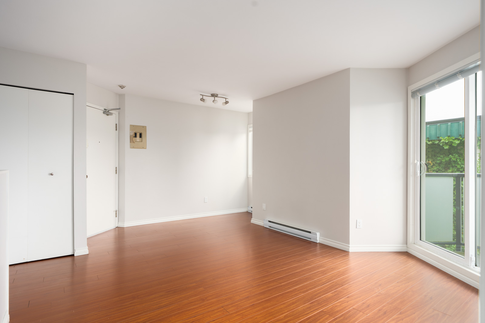 Bright room with light walls, wood floors, large windows, white closet, and exterior door on the 3rd floor in Vancouver.