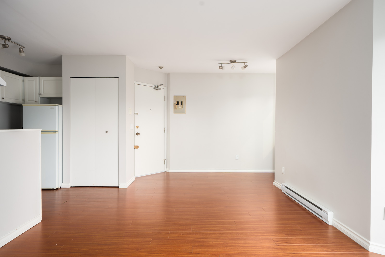 Unfurnished 3rd-floor apartment with white walls, wood floors, small kitchen, white fridge, and overhead lights in Vancouver.