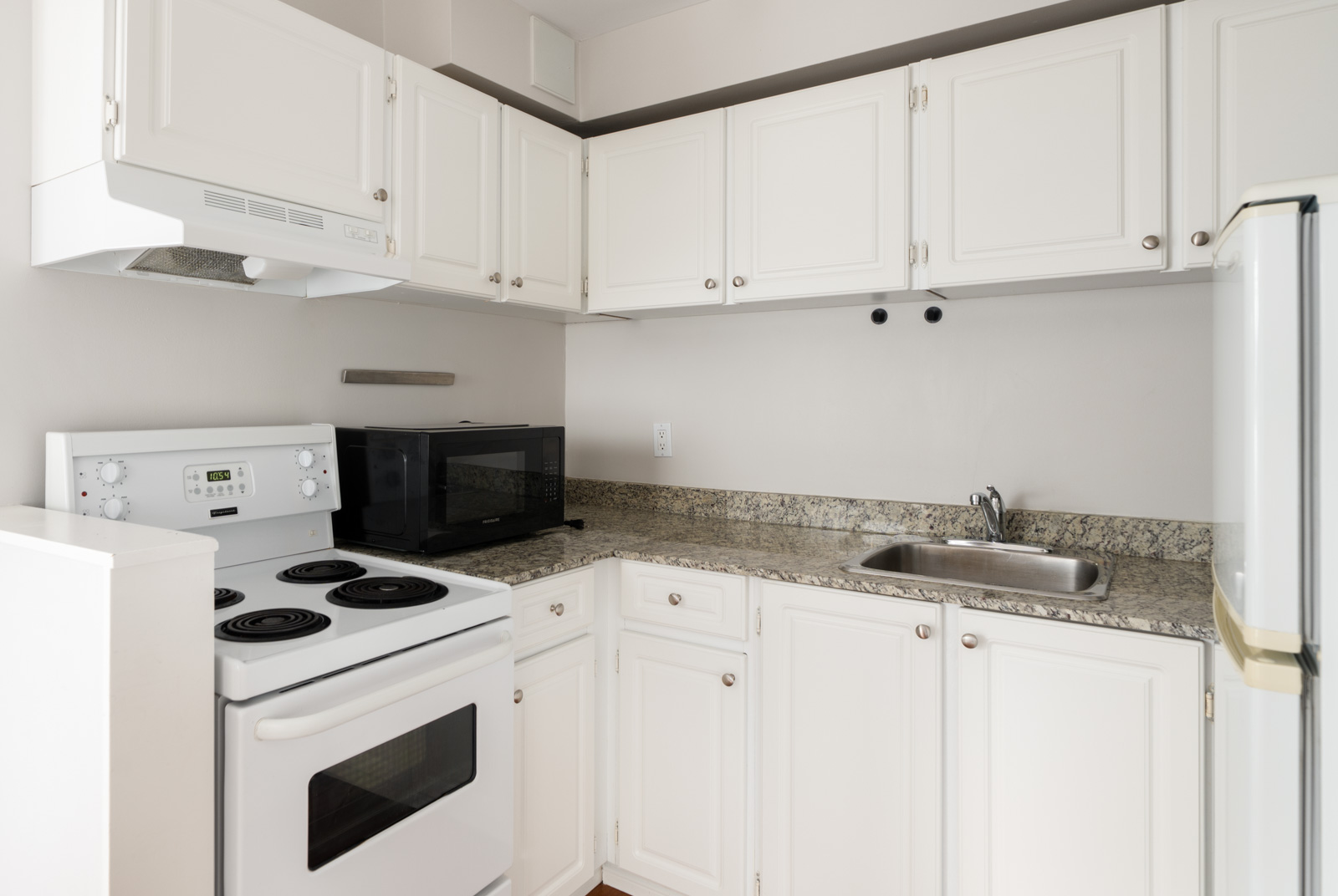 Compact Vancouver kitchen on West 5th Ave with white cabinets, granite counters, stainless sink, and light beige walls.