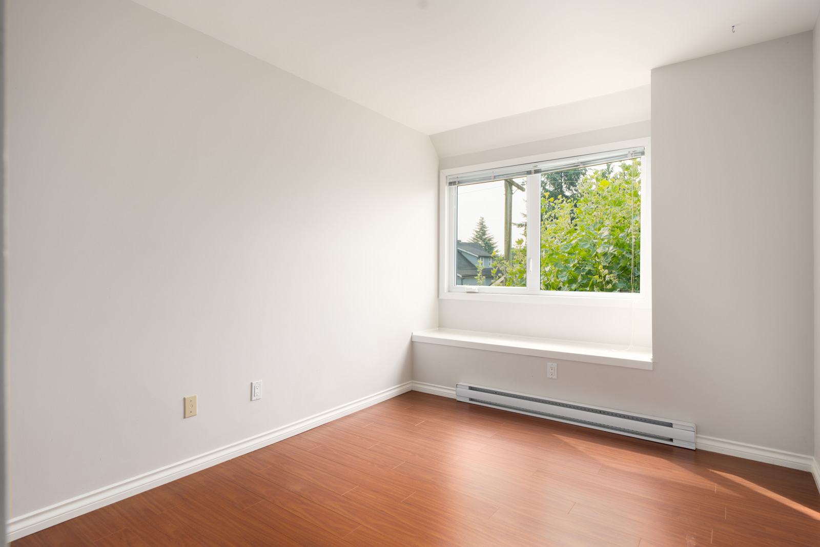 Empty room with pale walls, large window with white blinds, wood floors, baseboard heater below. 3rd floor, Vancouver.