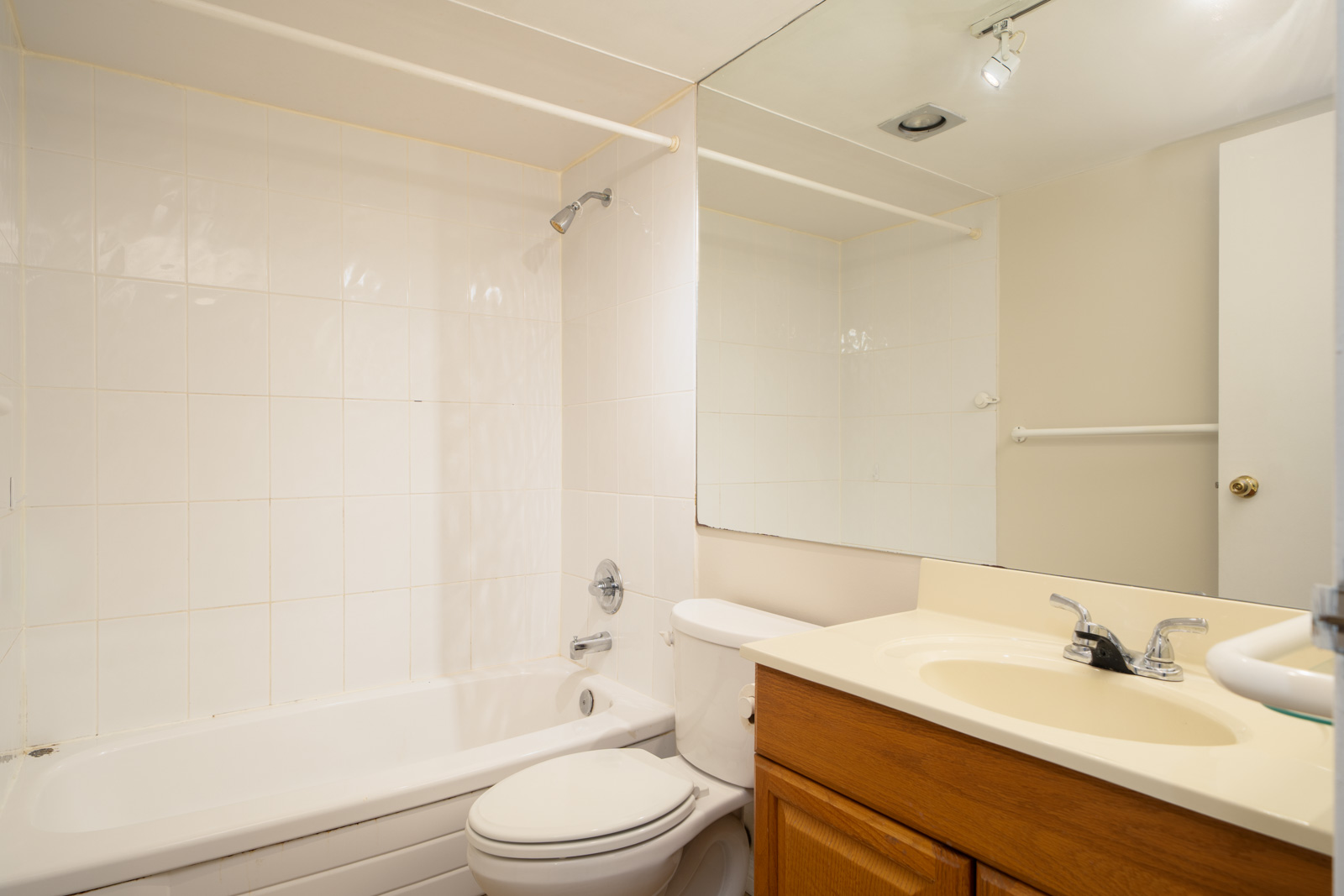 Bathroom on Fullerton Ave, Vancouver with a white tub-shower combo, toilet, light countertop, wood vanity, and large mirror.