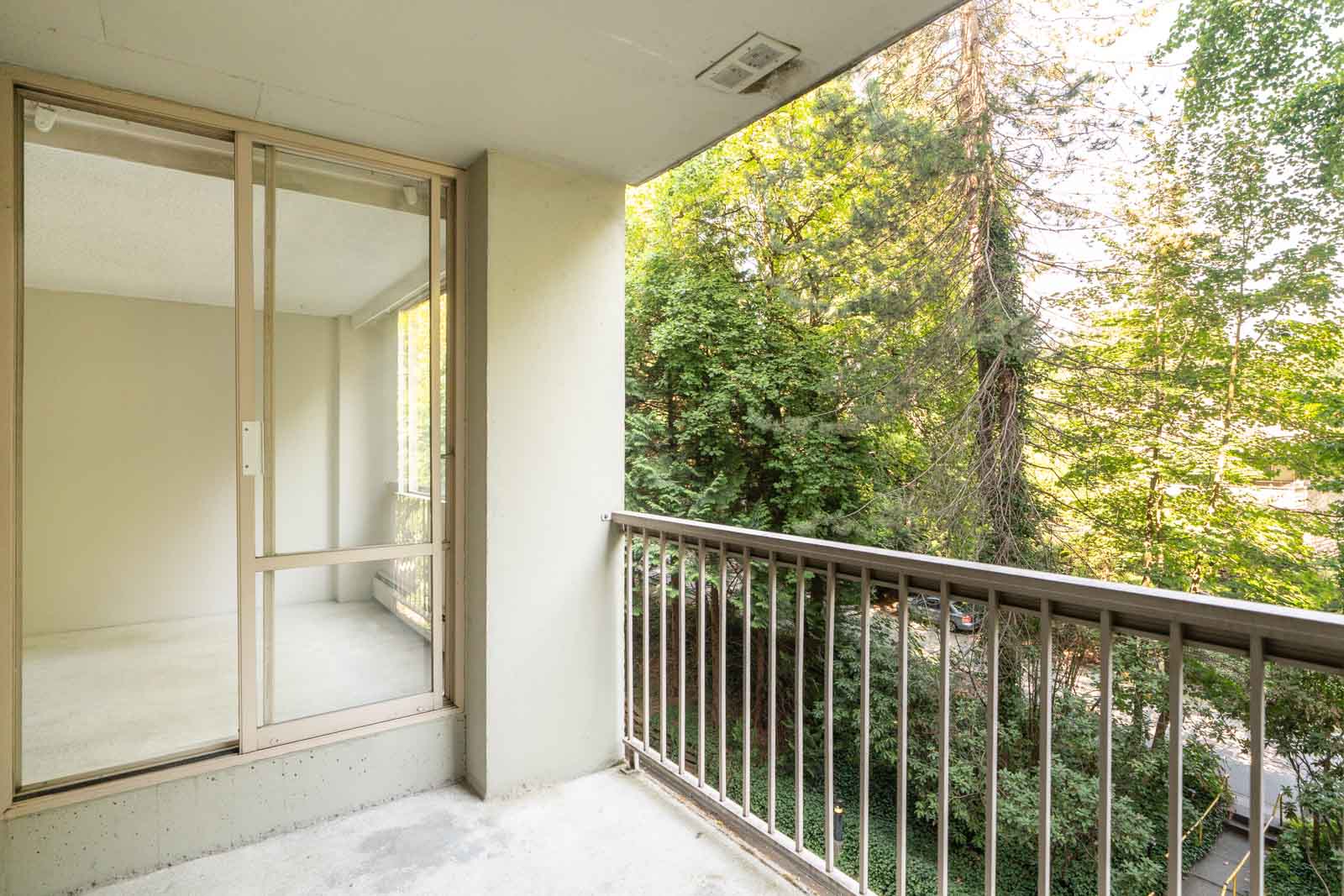 Unfurnished balcony with concrete floor, metal railing, beside sliding glass doors; green trees in Vancouver’s Fullerton Ave area.