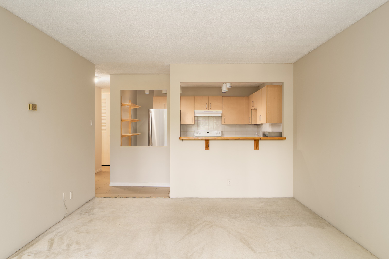Beige living room with carpet, open to a kitchen with light wood cabinets, stainless fridge, and breakfast bar on Fullerton Ave, Vancouver.