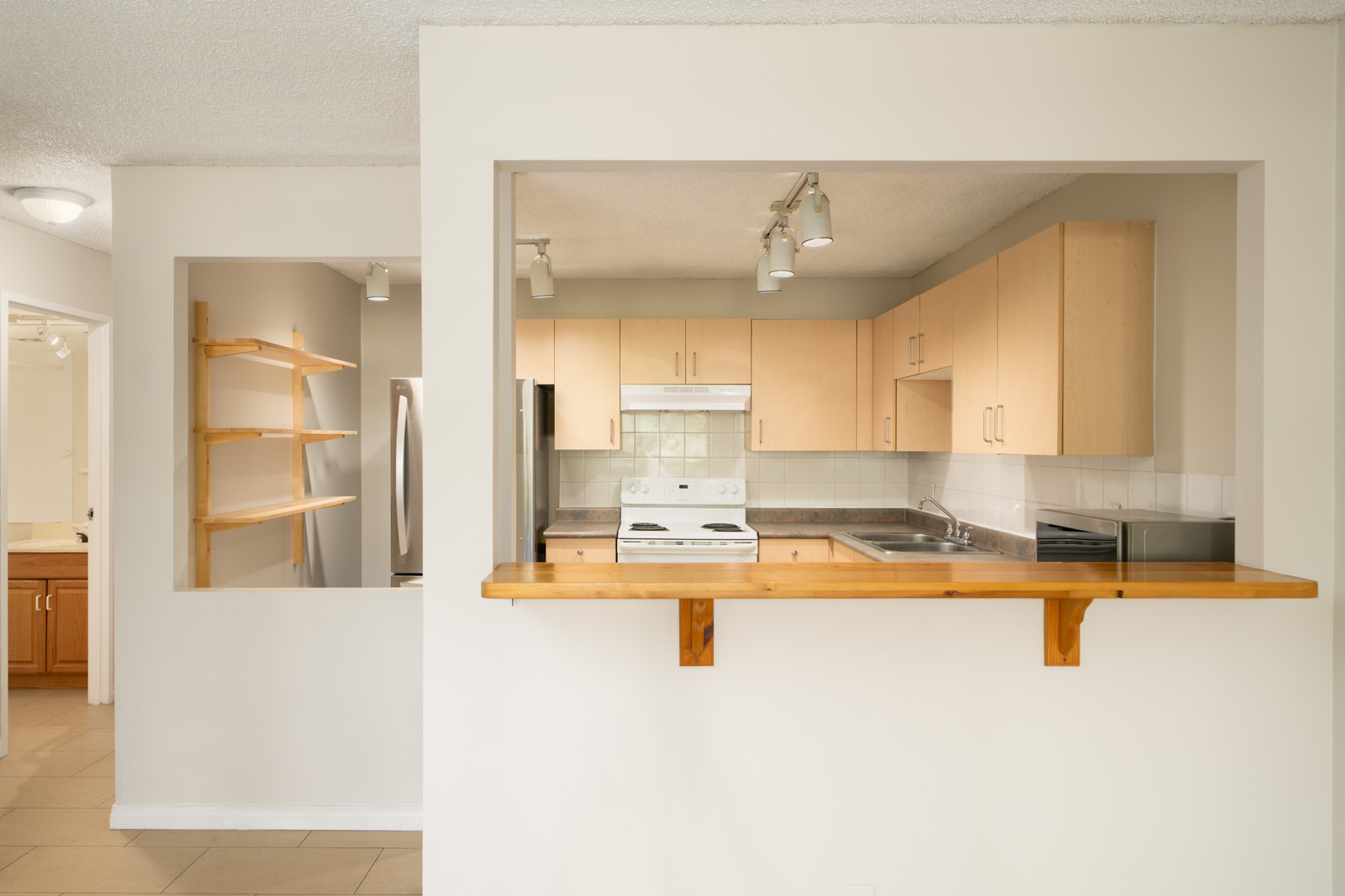 Modern kitchen on Fullerton Ave, Vancouver with light wood cabinets, white appliances, breakfast bar, open shelves, and tile floor.