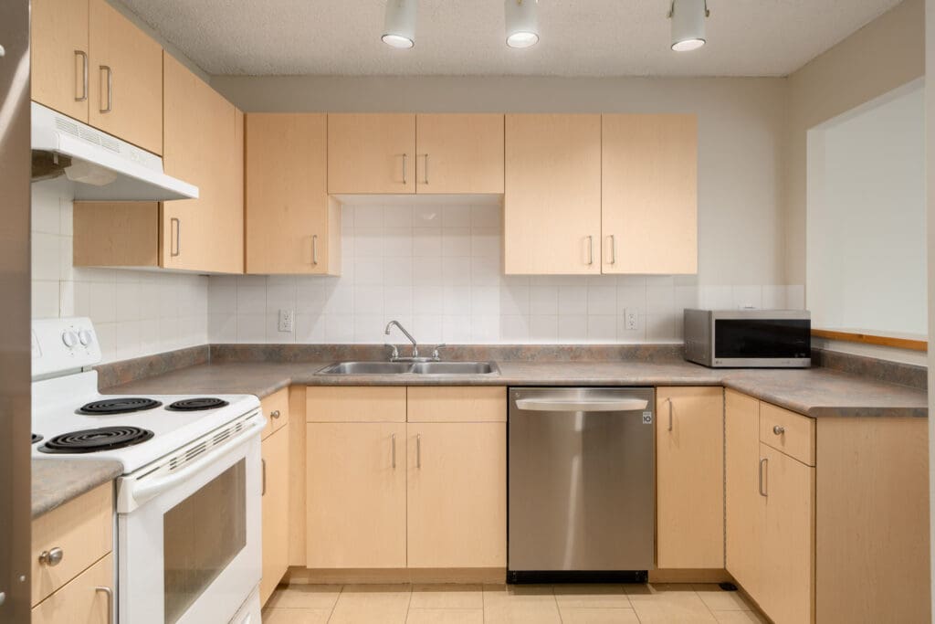 Modern kitchen on Fullerton Ave, Vancouver, with light wood cabinets, white tile backsplash, stainless dishwasher, and microwave.