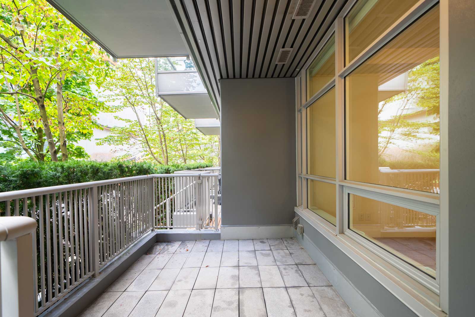 Balcony with metal railing, tiled floor, and large windows overlooking trees and greenery in Vancouver at 108 E 1st Ave.