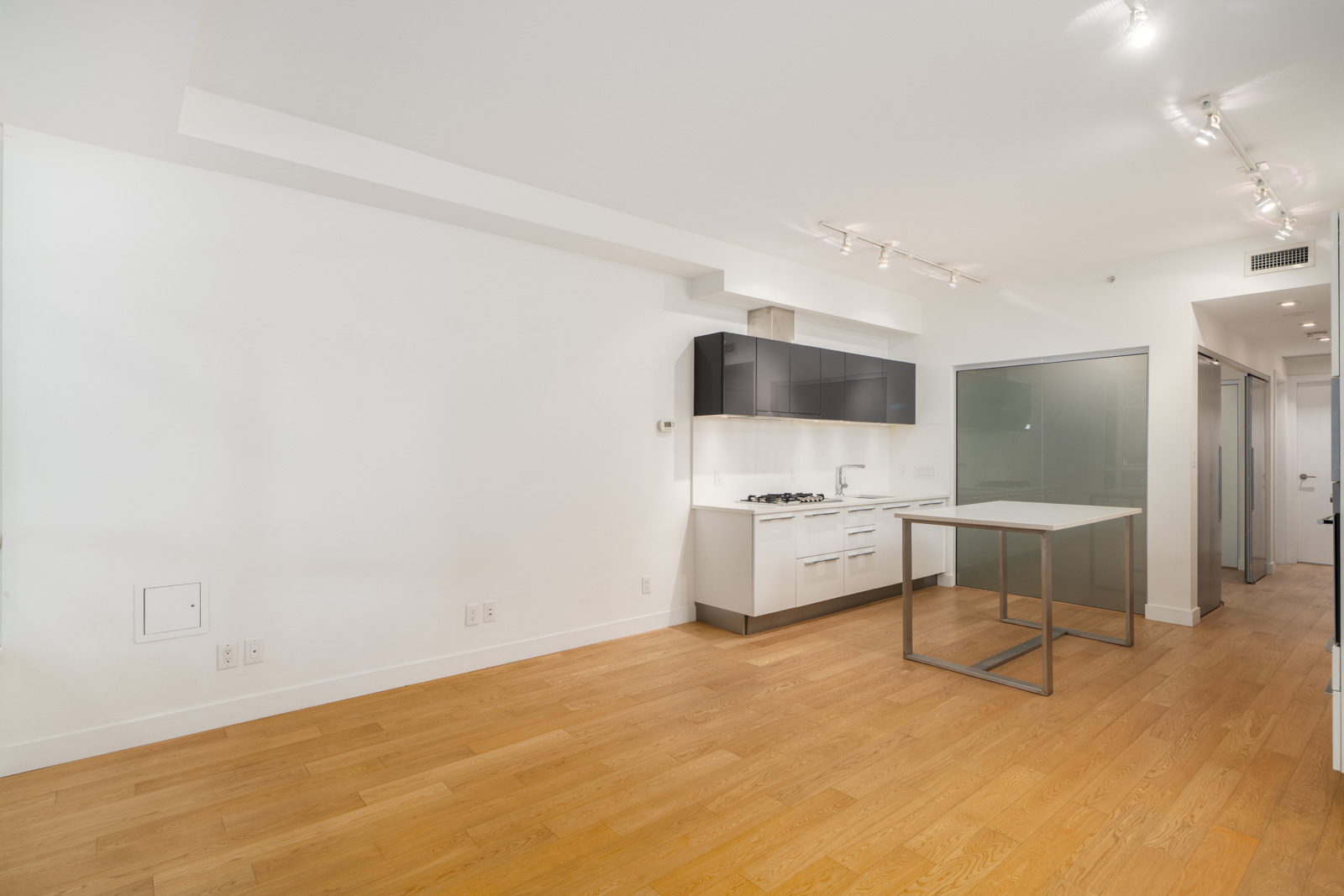 Modern kitchen with wood floors, white and black cabinets, stovetop, central island, glass wall and hallway; Vancouver, 108 E 1st Ave.