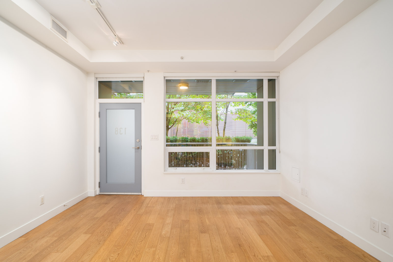 Empty room with hardwood floors, white walls, blue door labeled “801,” large windows showing trees and fence in Vancouver.