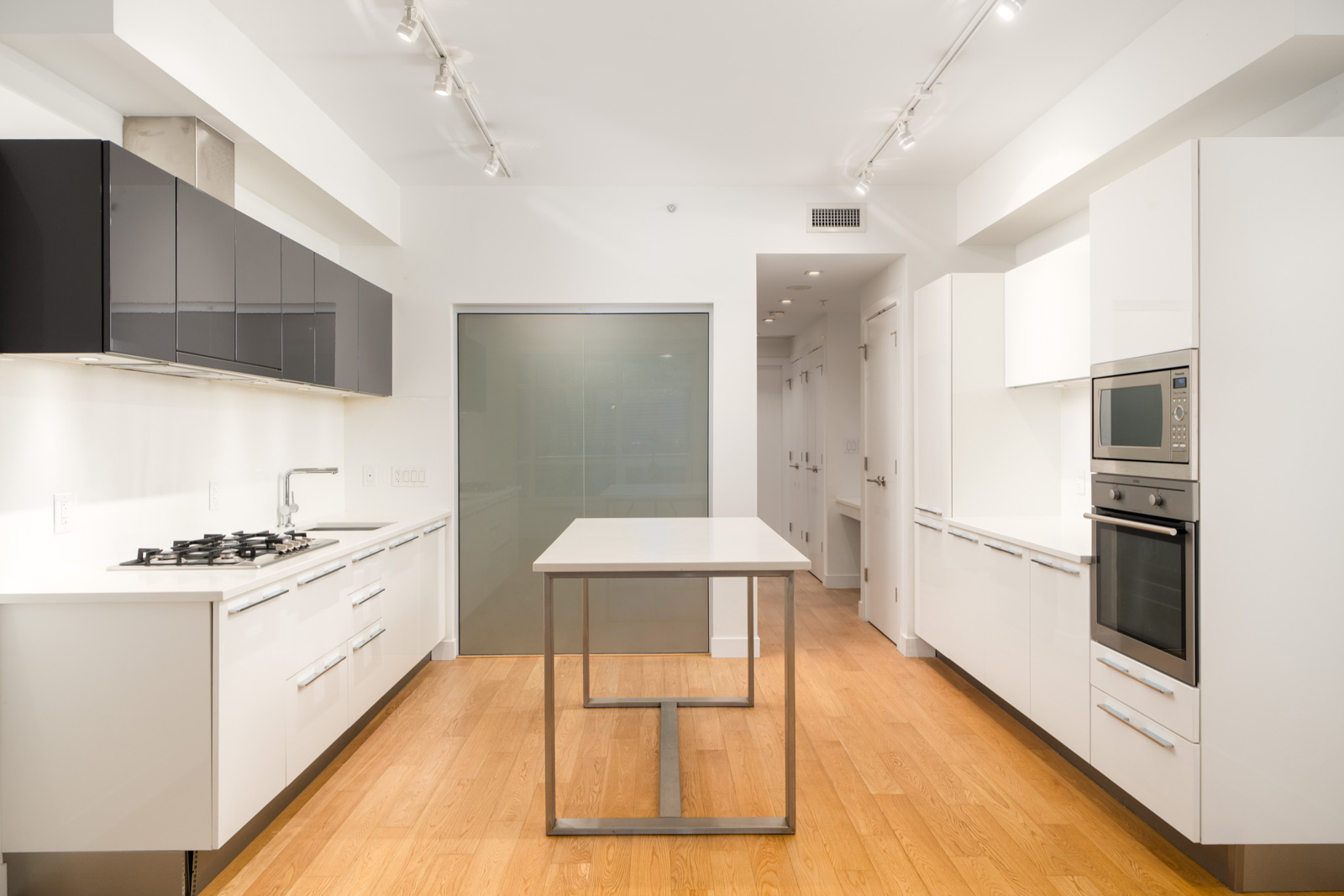 Modern kitchen with white cabinets, black upper cupboards, built-in oven, gas stove, island, and wood floors in Vancouver townhouse.
