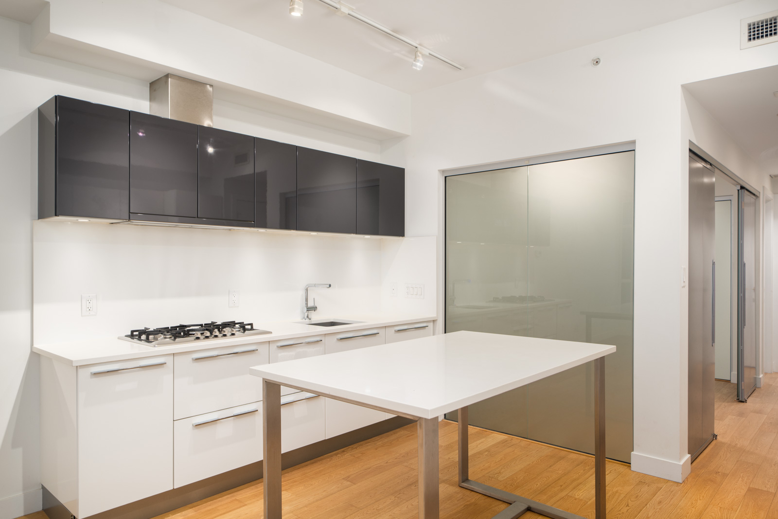 Modern kitchen at 108 E 1st Ave, Vancouver, with white cabinets, black uppers, built-in stove, range hood, and white island on wood floor.