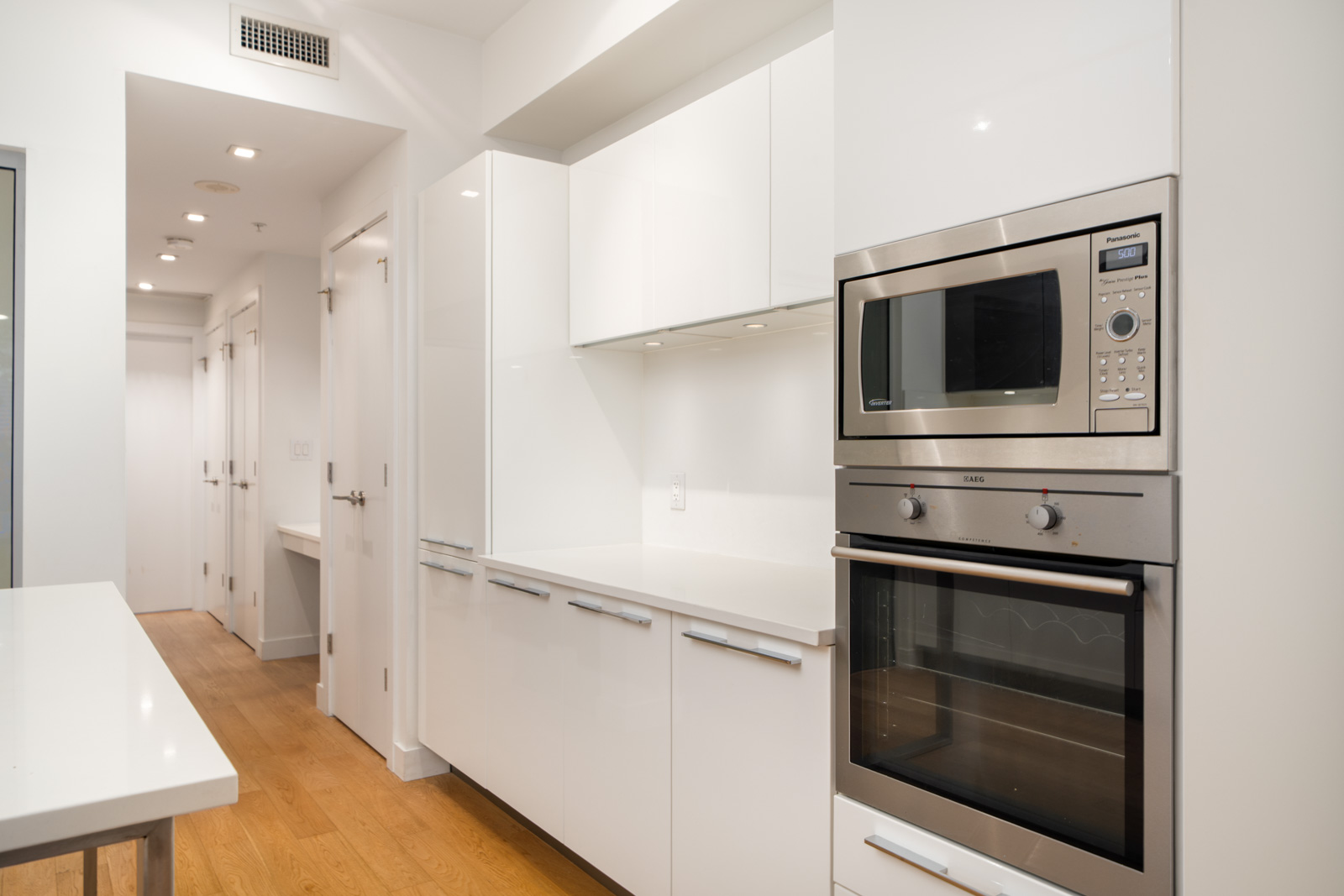 Modern kitchen at 108 E 1st Ave, Vancouver with white cabinets, stainless appliances, light wood floors, and white countertops.