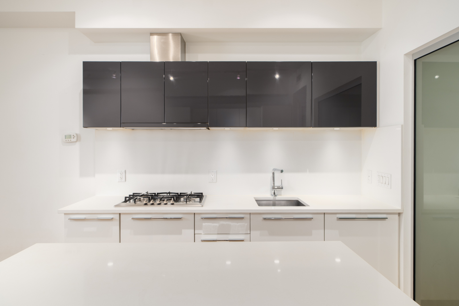 Contemporary kitchen at 108 E 1st Ave, Vancouver, with black upper cabinets, white lowers, gas stove, built-in oven, and sink.