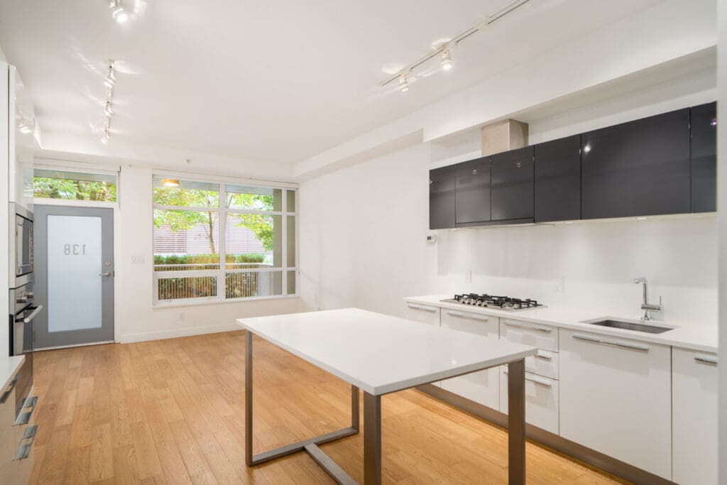 Modern kitchen in a Vancouver townhouse with white cabinets, black uppers, island, wood floors, large windows, and patio door.