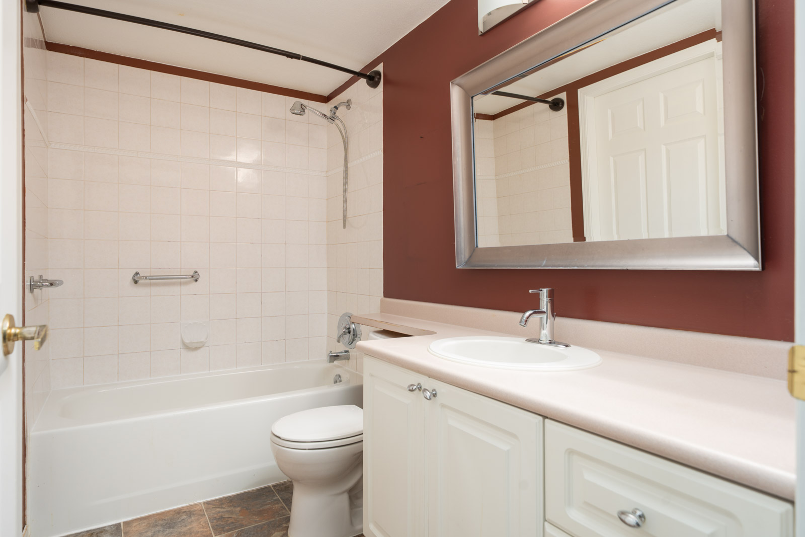 Bathroom on Triumph St, Vancouver with white tub, toilet, vanity, large mirror, maroon accent wall, tiled shower, and open door.