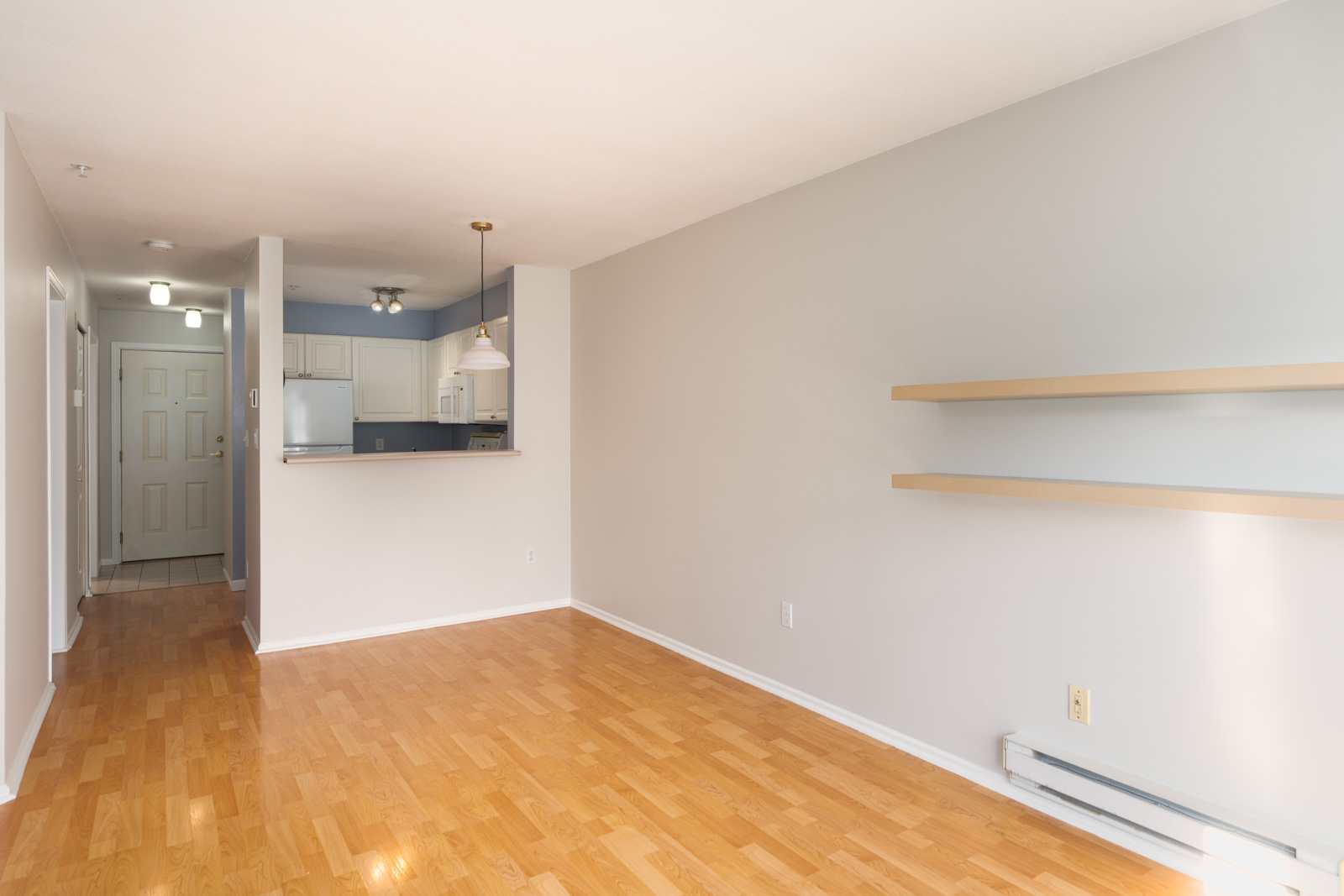 Unfurnished Triumph St, Vancouver apartment with light wood floors, off-white walls, shelves, and kitchen with white cabinets.