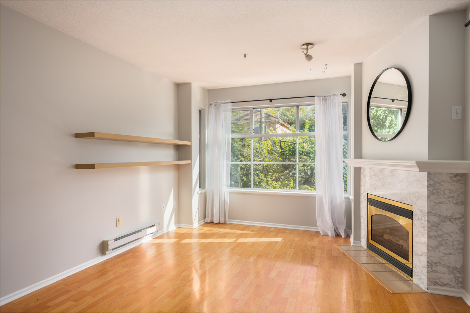 Bright 3rd floor living room in a Triumph St, Vancouver home with light wood floors, built-in shelves, large window, and fireplace.