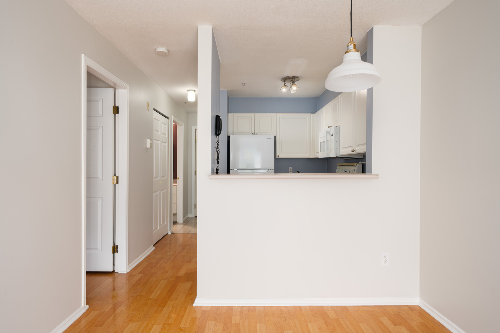 Small 3rd-floor kitchen with white cabinets, wood floors, and neutral walls, separated from hallway by half wall on Triumph St, Vancouver.