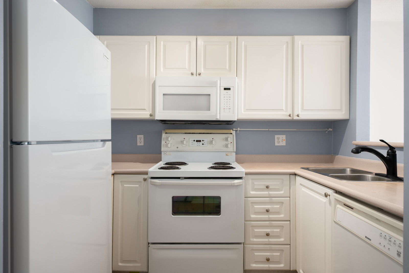 Kitchen on Triumph St, Vancouver with white cabinets, white appliances, and a stainless steel sink on a beige countertop.