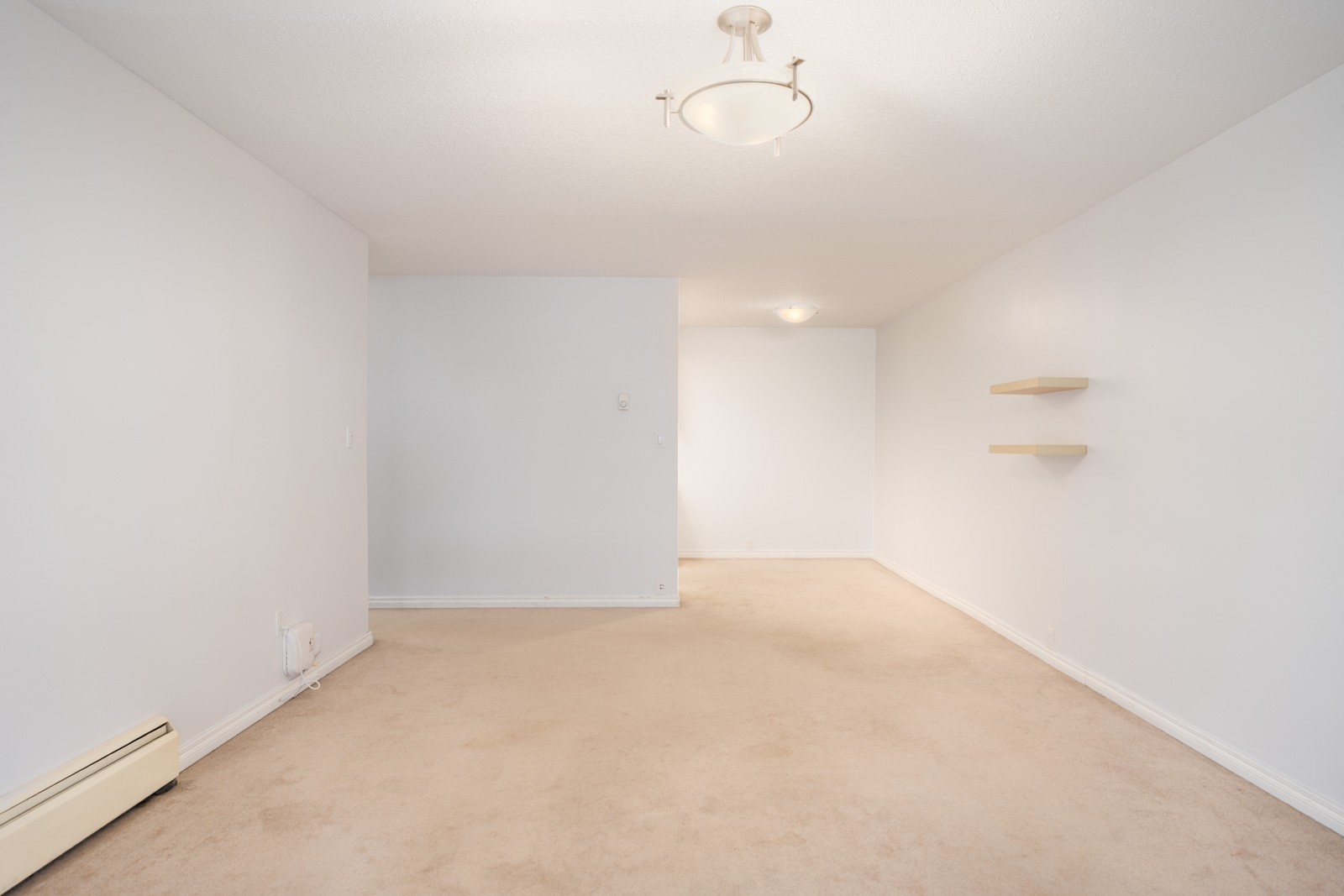 Empty room in Richmond at 6560 Buswell with beige carpet, white walls, ceiling lights, two shelves, and a baseboard heater.