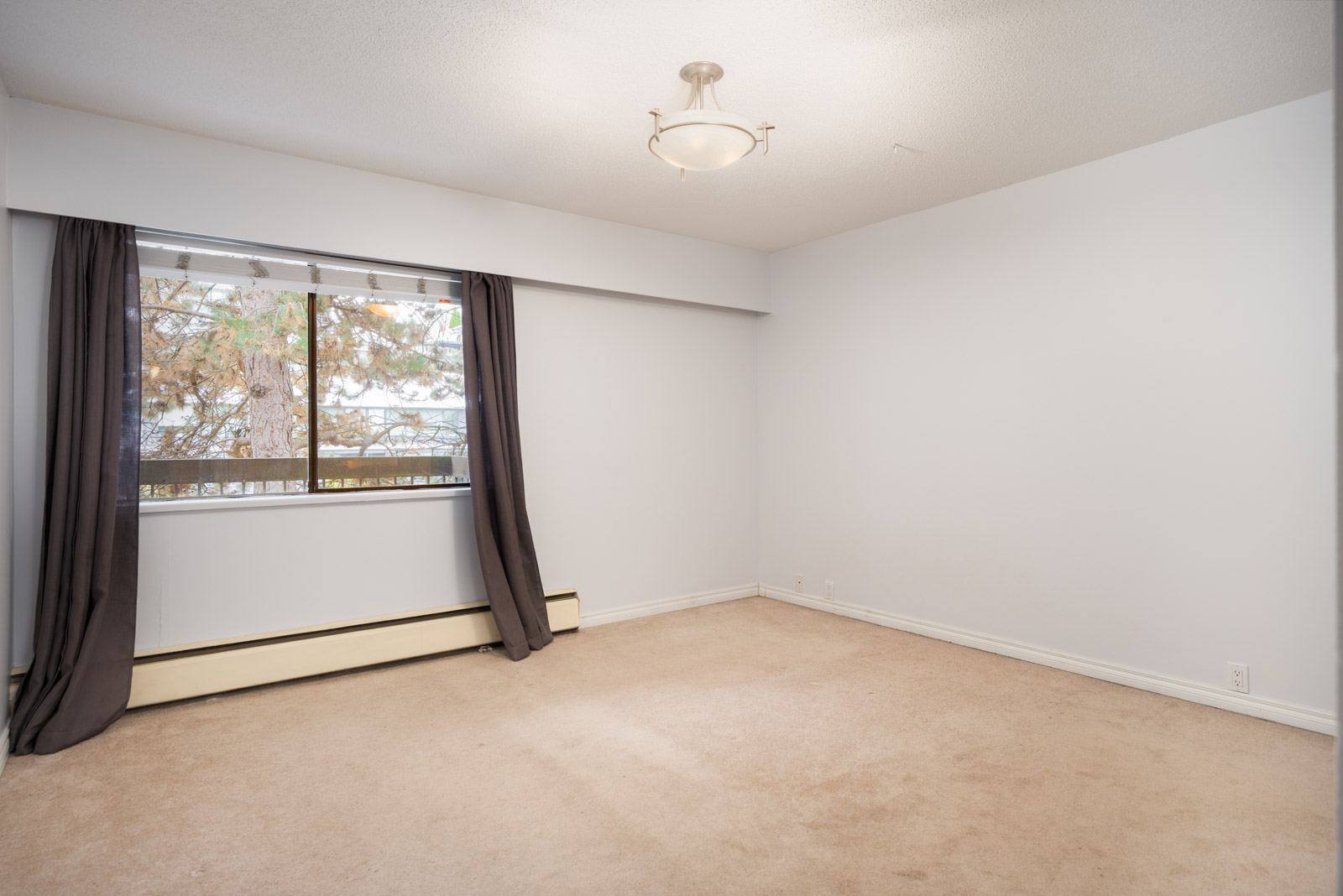 Carpeted room on Buswell in Richmond, 2nd floor, large window with dark curtains, white walls, ceiling light, baseboard heater.